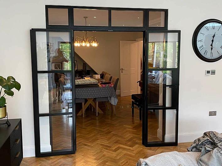 Fully open black Aluco steel-look double doors with a top panel, connecting a living room to a dining area