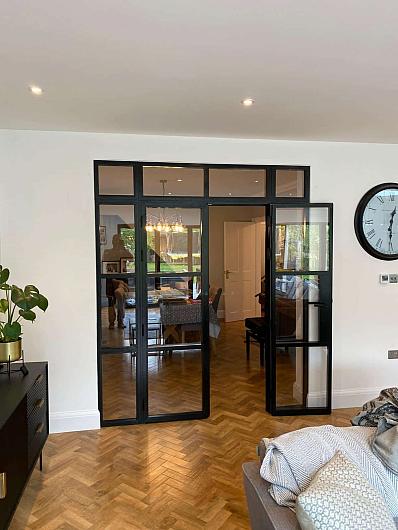 Black Aluco steel-look double doors with one door open, viewed from a living room with herringbone floors