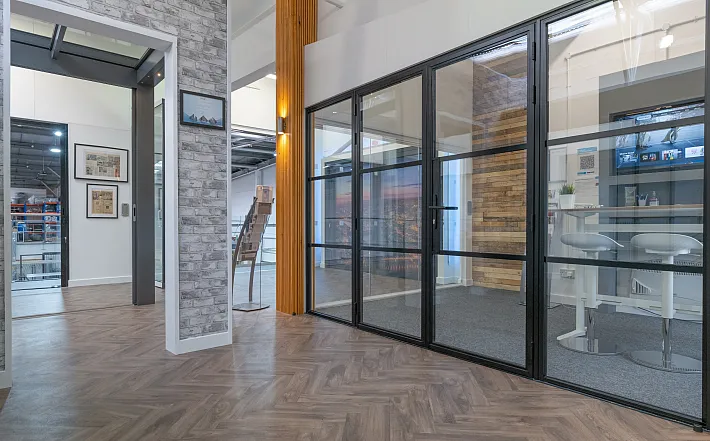 Showroom displaying a black steel-replacement french door and screen system with horizontal bars on a herringbone floor
