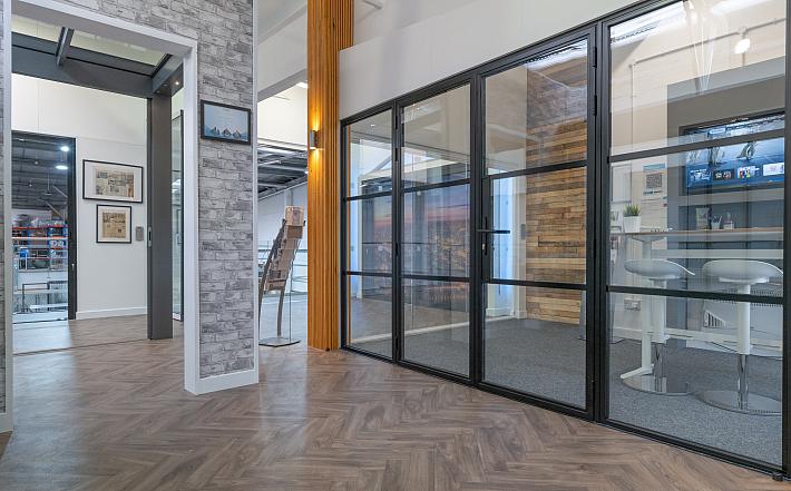 Showroom displaying a black steel-replacement french door and screen system with horizontal bars on a herringbone floor
