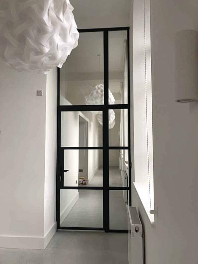 A tall, black Aluco steel-look internal door and screen with a grid pattern, installed in a narrow white hallway.