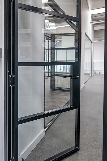 Open black Aluco steel-look internal door with horizontal bars, showing the lever handle and view into another showroom area