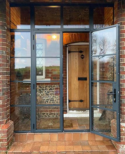 Dark grey steel-look porch door and screen with grid pattern, set on a brick house, with the door open to a wood front door