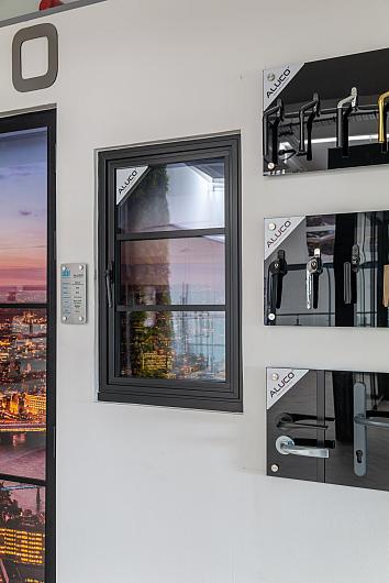 Aluco showroom display showing a black steel-look sample window with horizontal bars, next to various Aluco handle options