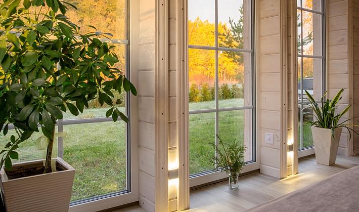 A bright room with white wood walls and large, white aluminium windows with a grid pattern, looking out onto a sunny field