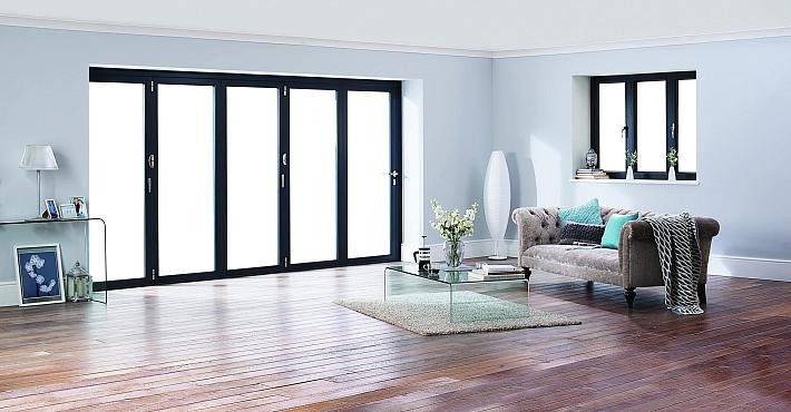 Minimalist living room with dark grey five-panel Origin bifold doors and a matching three-panel Origin window