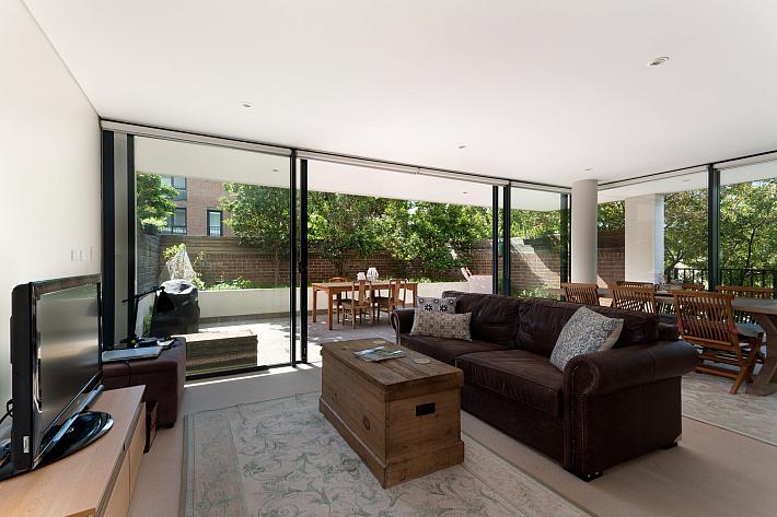 Bright living room with a brown leather sofa and large black sliding doors open to a sunny patio with a dining table