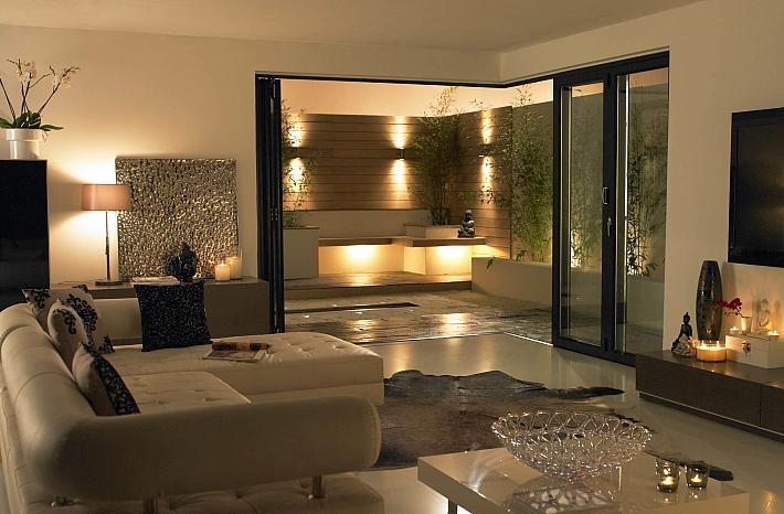 Modern living room at night with black open-corner bifold doors, leading out to a lit contemporary patio