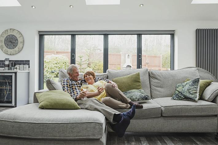 Couple relaxing on a sofa with wine in front of a large, closed dark grey bifold door in a modern living room.