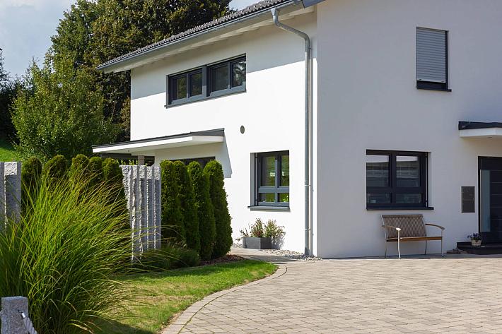 A modern white house with a paved driveway, featuring multiple dark grey aluminium casement windows