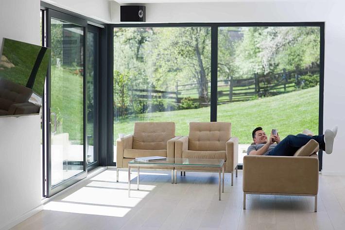 Man relaxing on a couch in a modern living room with large, black slim sliding doors open to a sunny garden