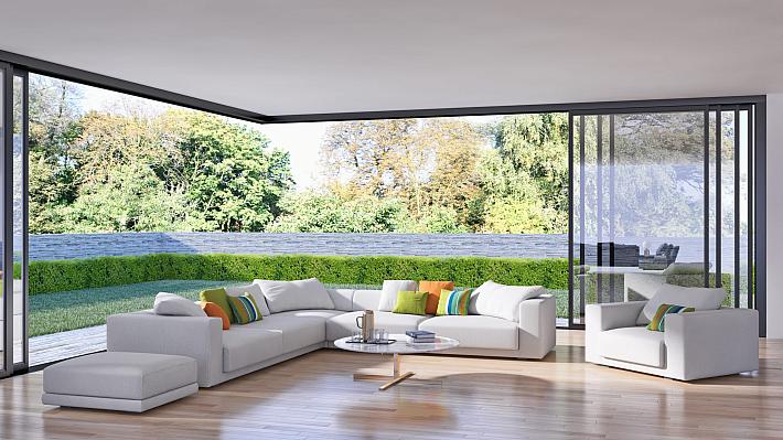 Modern living room with a white sectional sofa and large black open-corner sliding doors leading out to a garden with trees