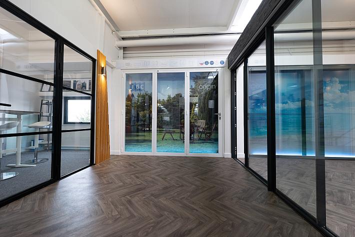 A bright FGC showroom with herringbone floors, displaying white Origin bifold doors and black internal screens