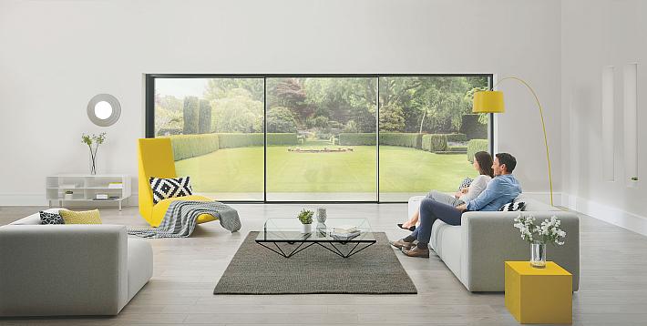 Two people sit on a sofa, looking out of a large, floor-to-ceiling slimline sliding door onto a manicured lawn.