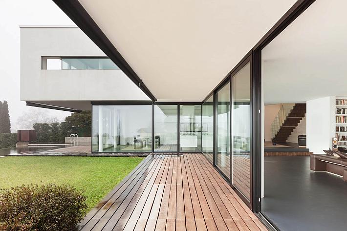 Modern white house with a wooden deck, black-framed sliding glass doors, and a seamless indoor-outdoor living space