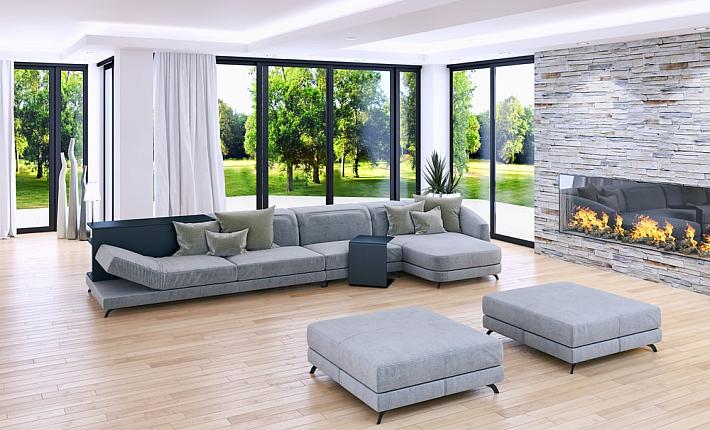 Modern living room with a grey sofa and stone fireplace, surrounded by tall, black-framed bifold doors showing a green yard