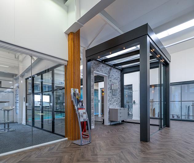 Showroom interior with herringbone floor, a large grey garden room display, and a black steel-look screen on the left