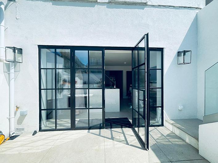 Black steel-look French doors set in a white wall, with one door open, leading from the patio into a bright kitchen