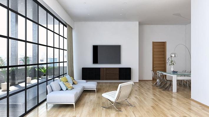 A modern, open-plan living room with a large, black steel-look screen and window wall overlooking a city balcony
