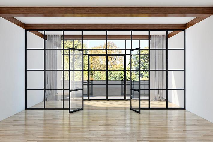 A large black steel-look glass wall with a grid pattern and open double doors, in an empty room with wooden floors