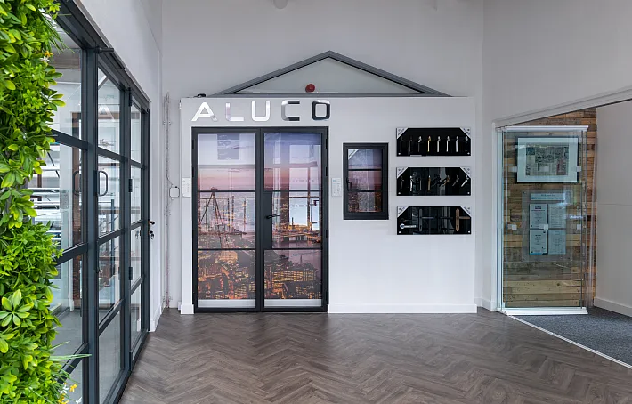 Wide view of the Aluco showroom display wall, featuring steel-look doors, a window, handle options, and a green wall