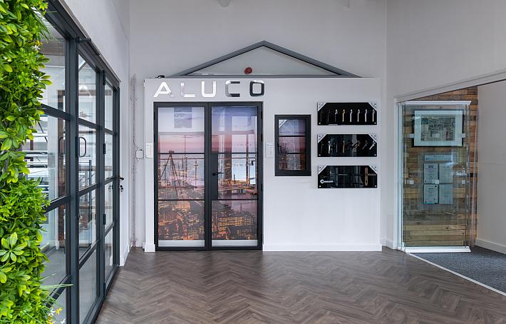 Wide view of the Aluco showroom display wall, featuring steel-look doors, a window, handle options, and a green wall