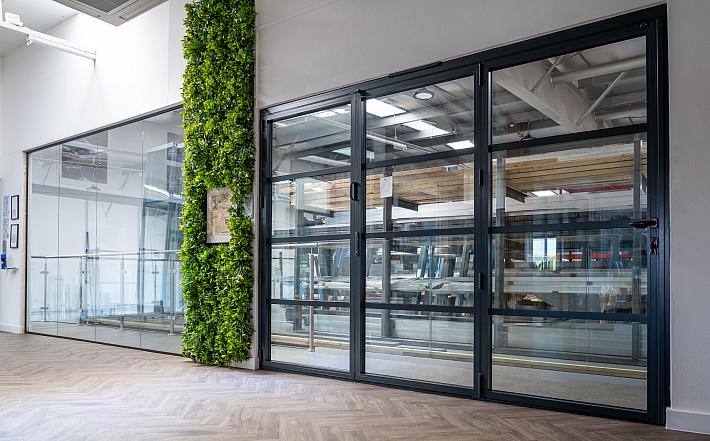 Large black steel-look bifold door with horizontal bars, installed in a showroom with herringbone floors and a green wall
