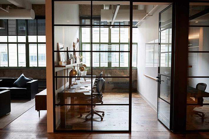 A modern office with a black steel-look glass screen and a matching door, separating a hallway from a desk area