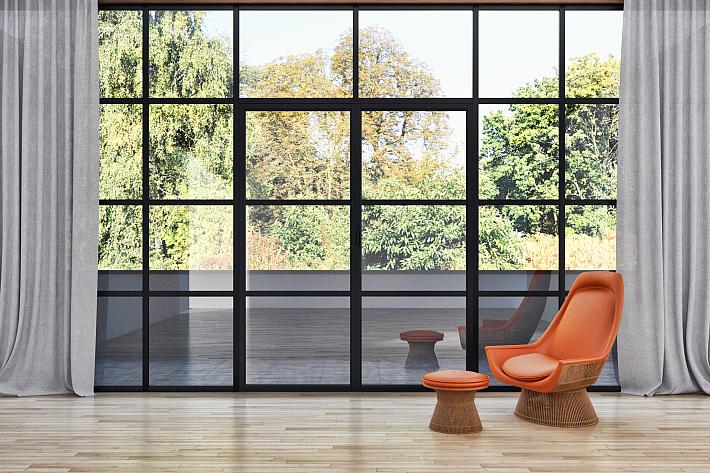 Large black steel-look window wall with a grid pattern, in a modern room with wood floors and an orange chair