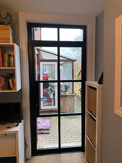 Interior view of a closed, single black steel-look door with a grid pattern, leading from a room out to a brick patio