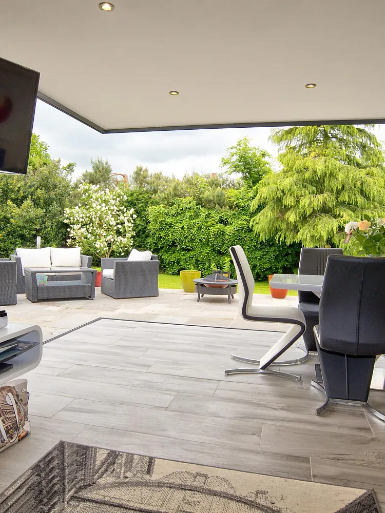 Modern dining room with bifold doors fully open, showing a seamless transition to an outdoor patio with garden furniture