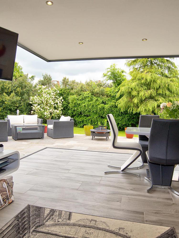 Modern dining room with bifold doors fully open, showing a seamless transition to an outdoor patio with garden furniture