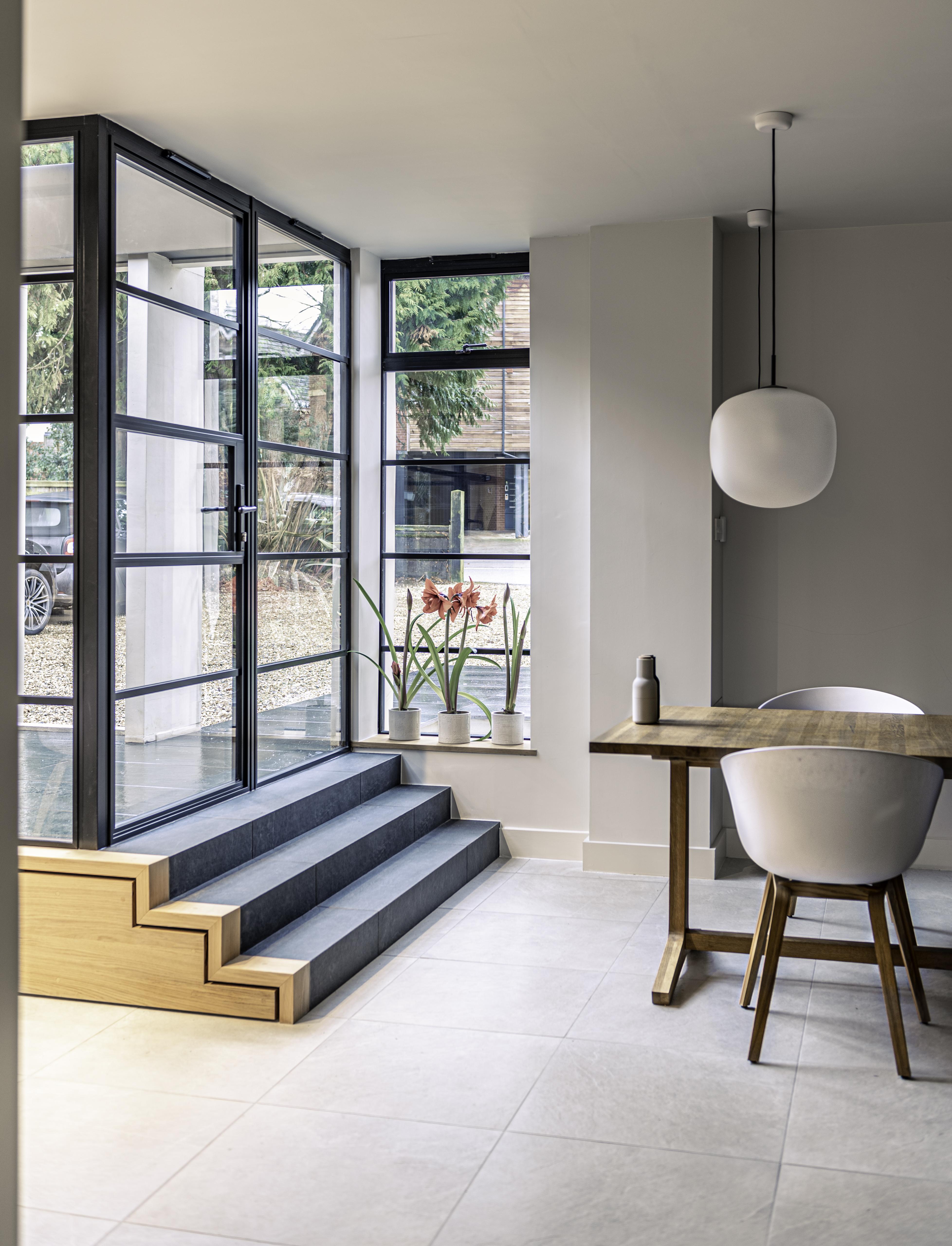 Modern dining area with steps leading up to a black steel-look door and window, showing amaryllis flowers on the sill