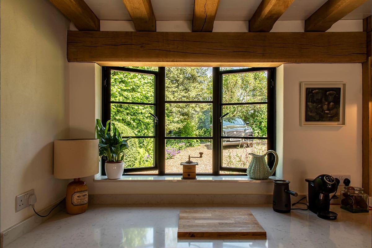 black, three-panel steel-replacement window with traditional handles, looking out onto a garden and driveway