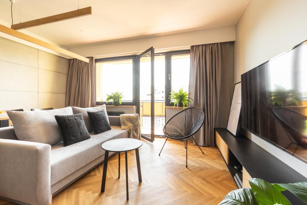 Living room with herringbone floors and a set of open double doors leading out onto a sunny balcony
