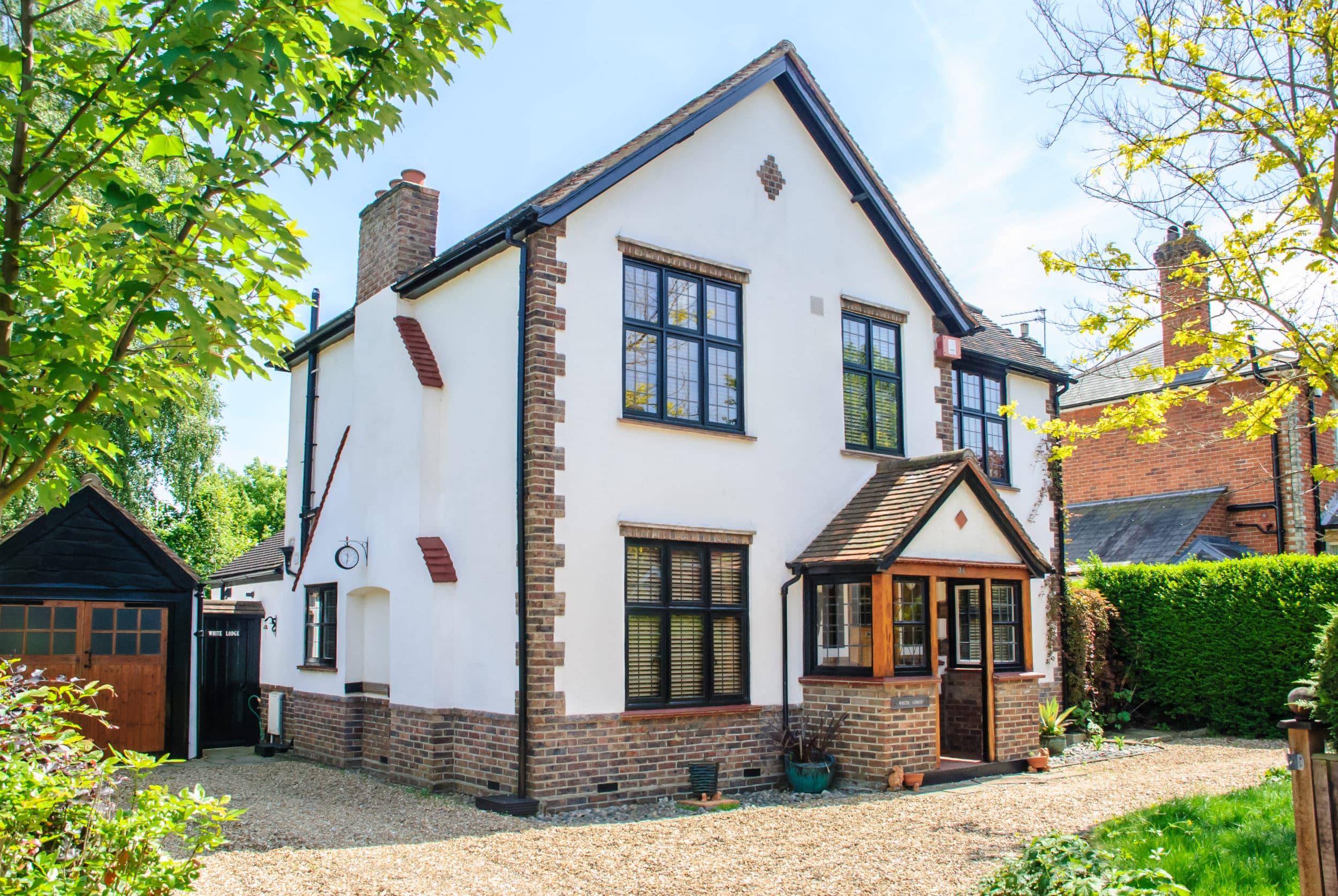 A white house with brick quoins, featuring black aluminium windows with a traditional leaded-style grid.