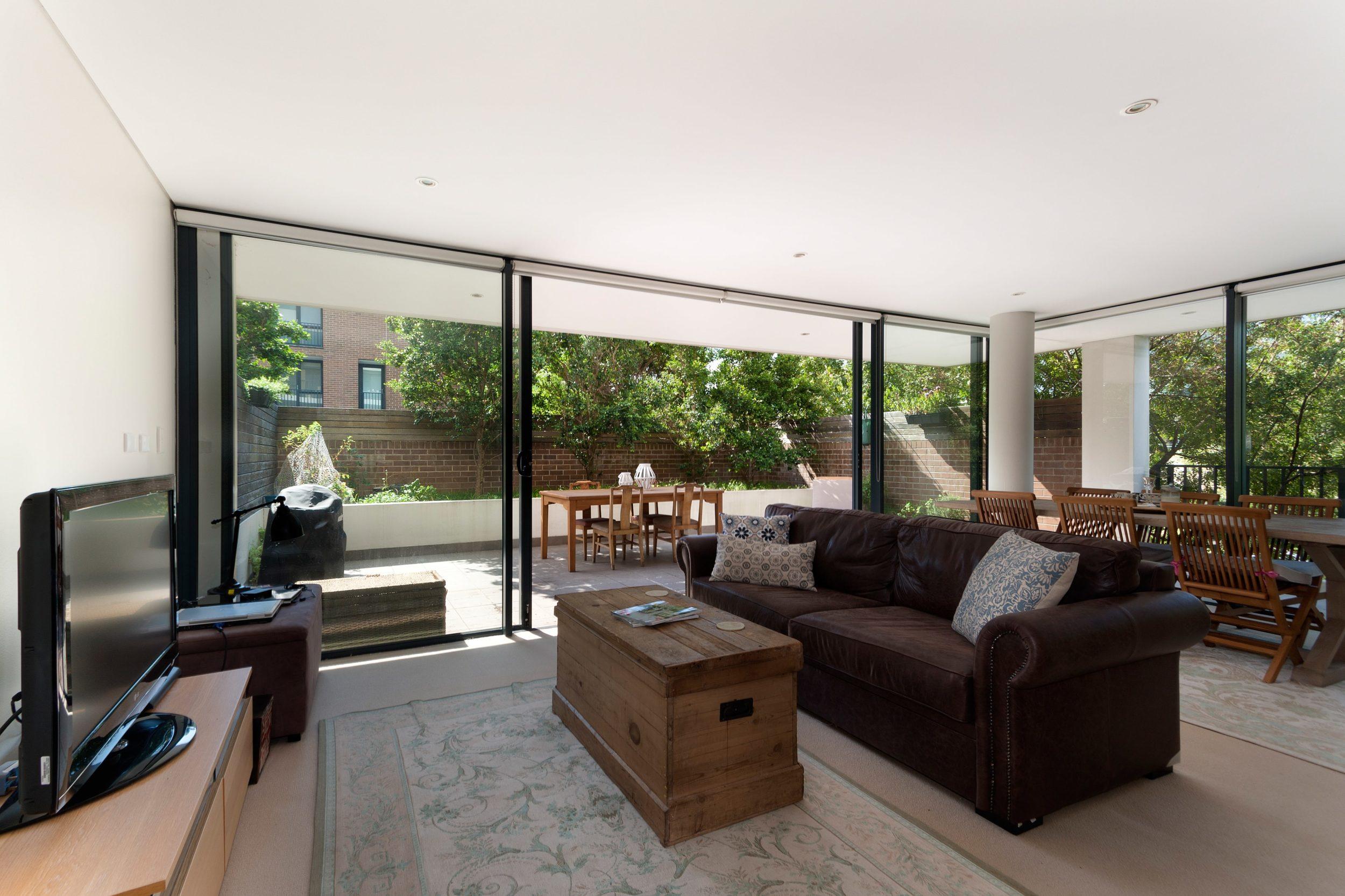Bright living room with a brown leather sofa and large black sliding doors open to a sunny patio with a dining table