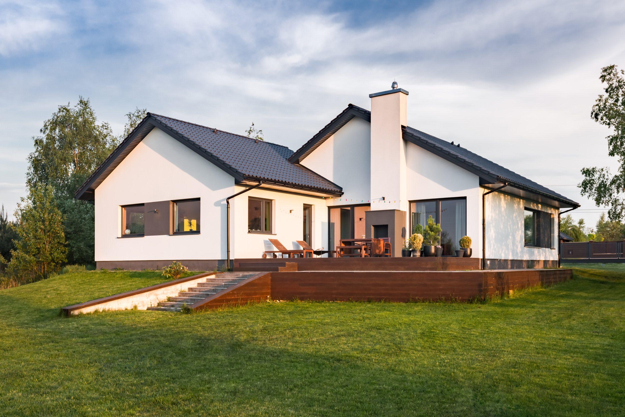 The back of a modern white house at sunset, showing a large wooden deck and several dark-framed aluminium windows