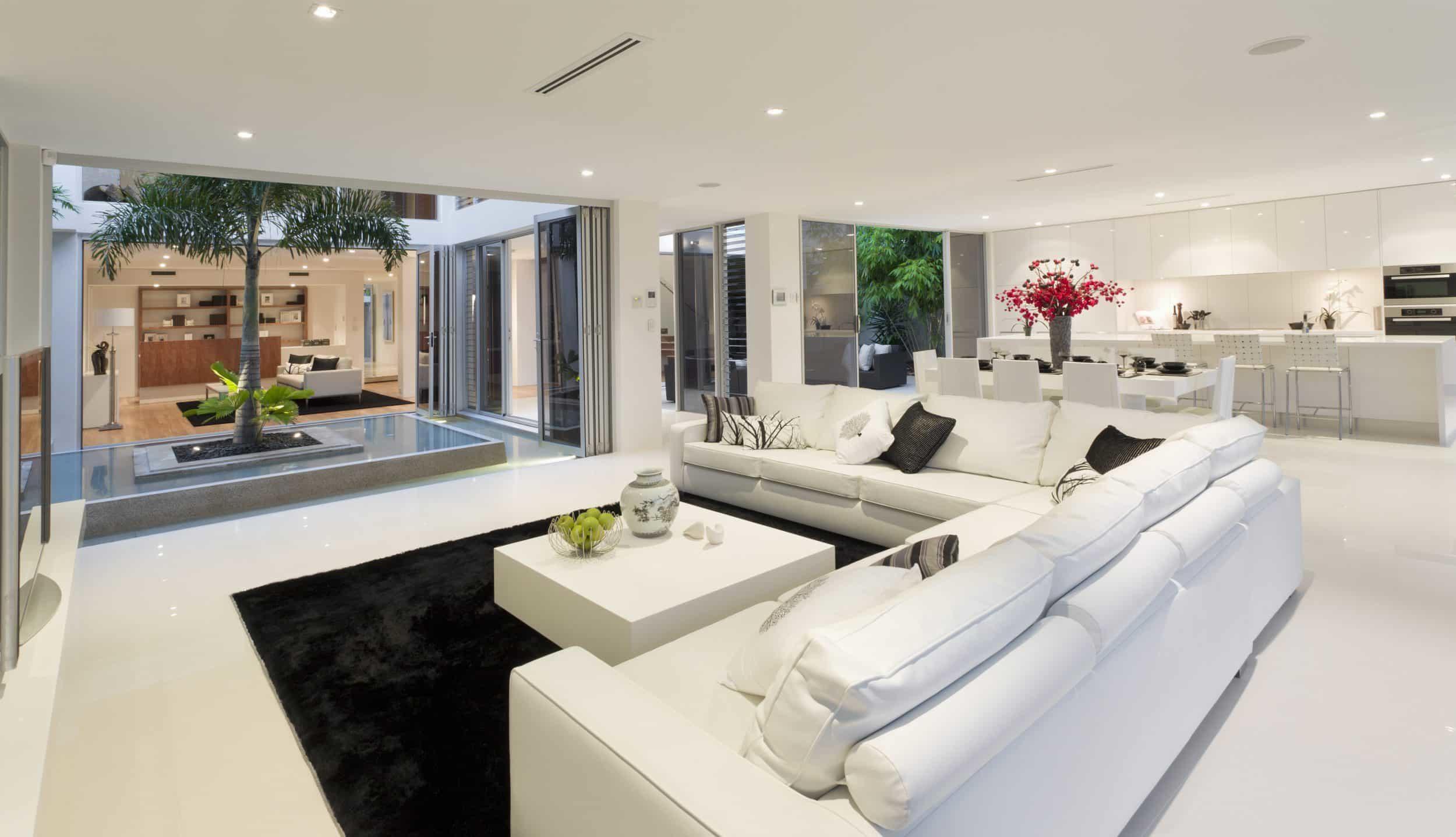 "Luxurious living room with white sofas and Origin OB-72 bifold doors open to an internal courtyard with a palm tree