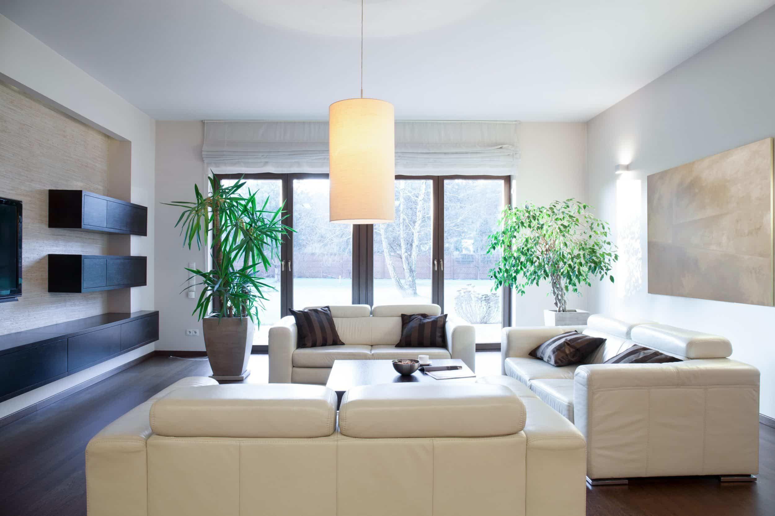 A modern living room with white leather sofas and dark-framed double doors in the background leading to a garden.