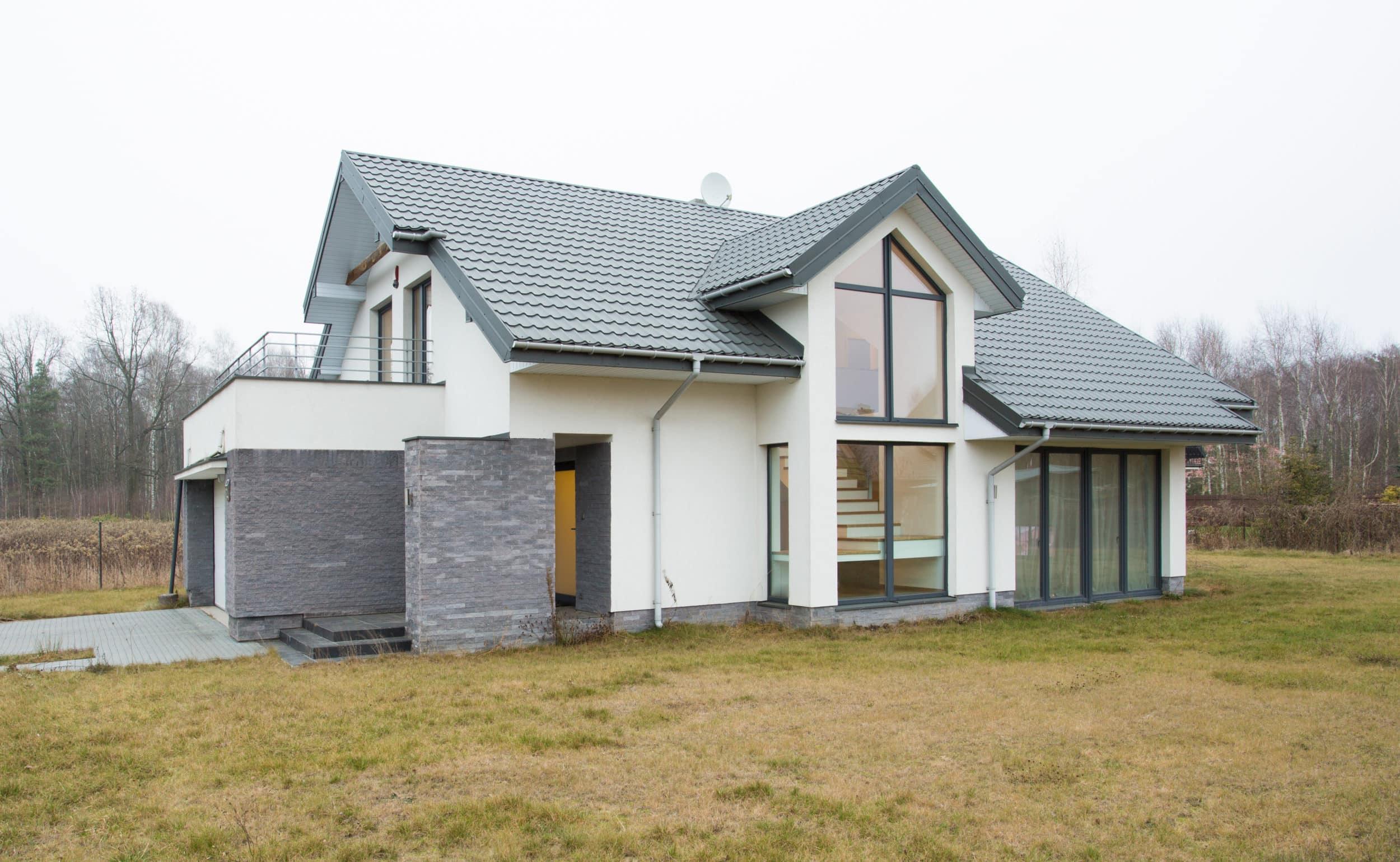 A modern white house with large, dark-framed aluminium windows, including a tall corner window and sliding patio doors