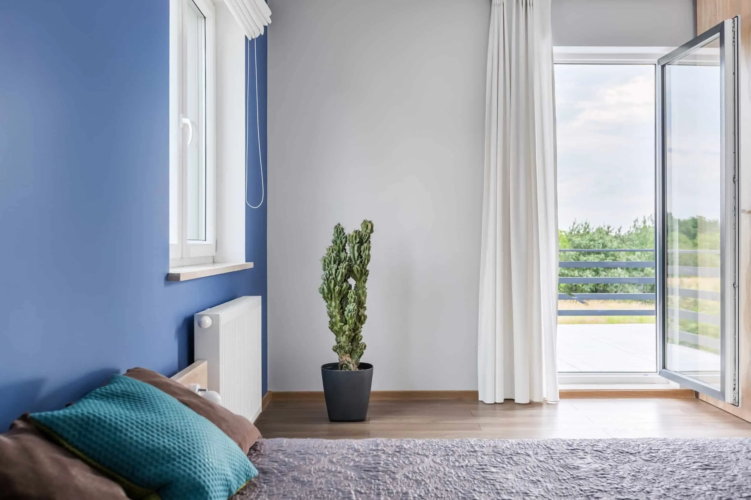 A bedroom with a blue wall and a single, full-glass door open to a balcony with a glass railing