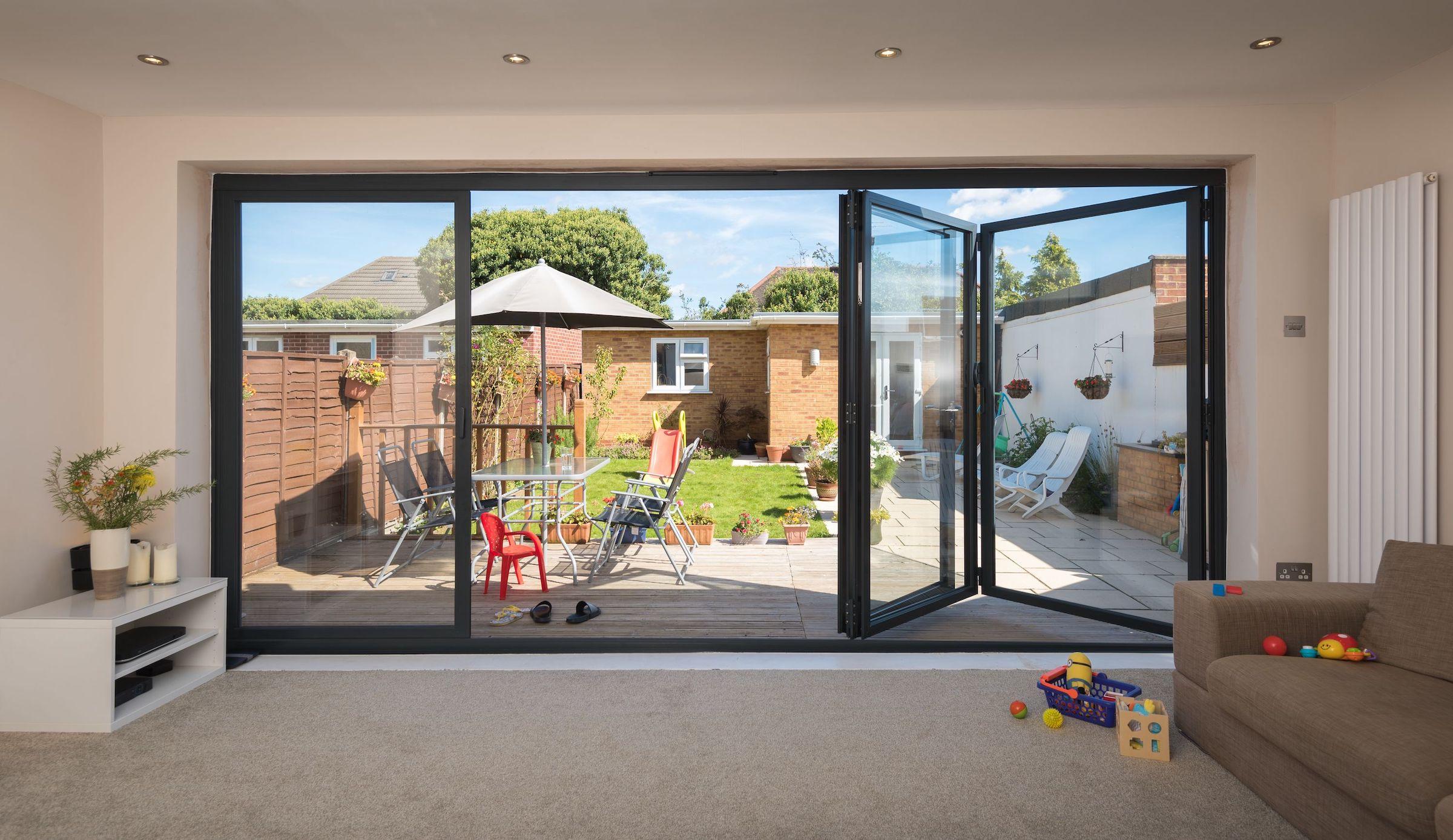 Dark grey Origin OB-49 bifold doors partially open, viewed from a living room, looking out onto a sunny garden deck