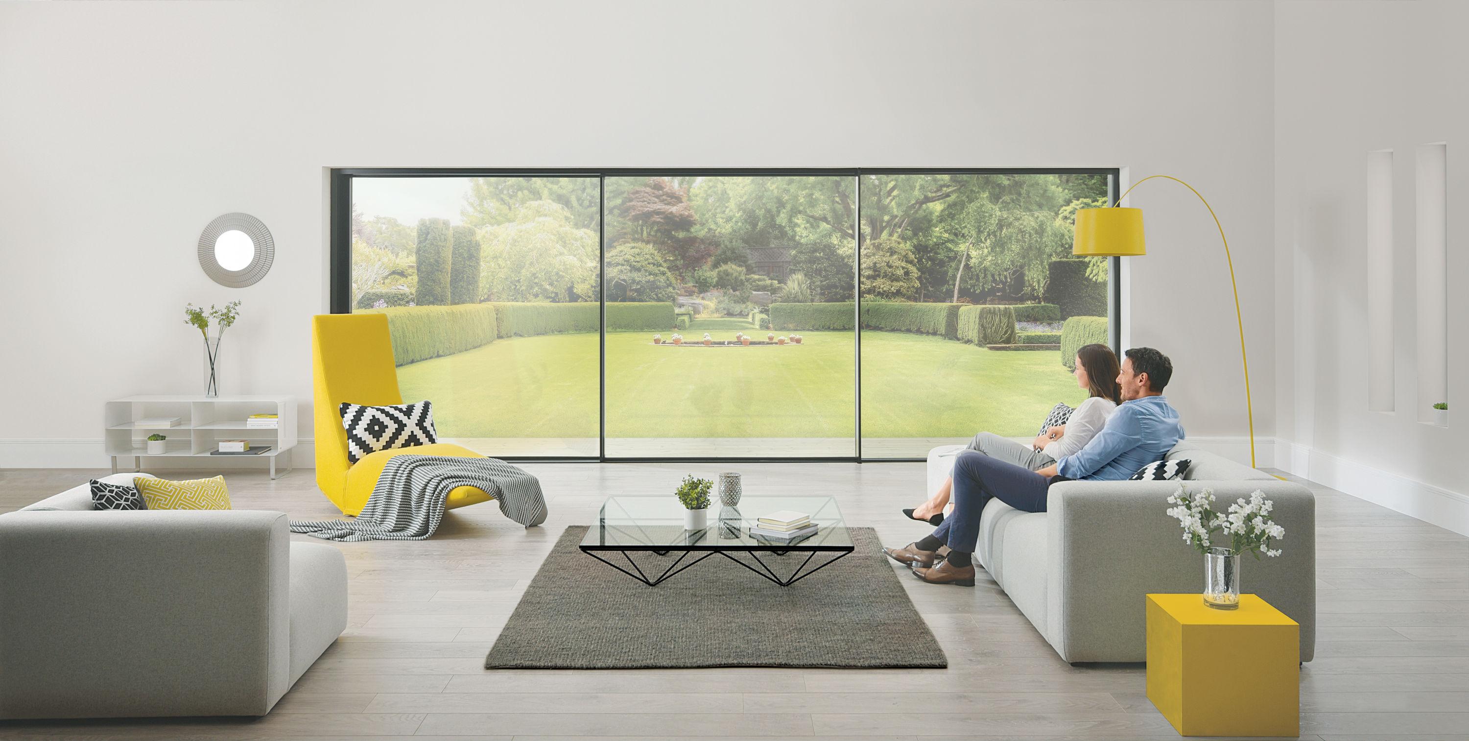 Two people sit on a sofa, looking out of a large, floor-to-ceiling slimline sliding door onto a manicured lawn.