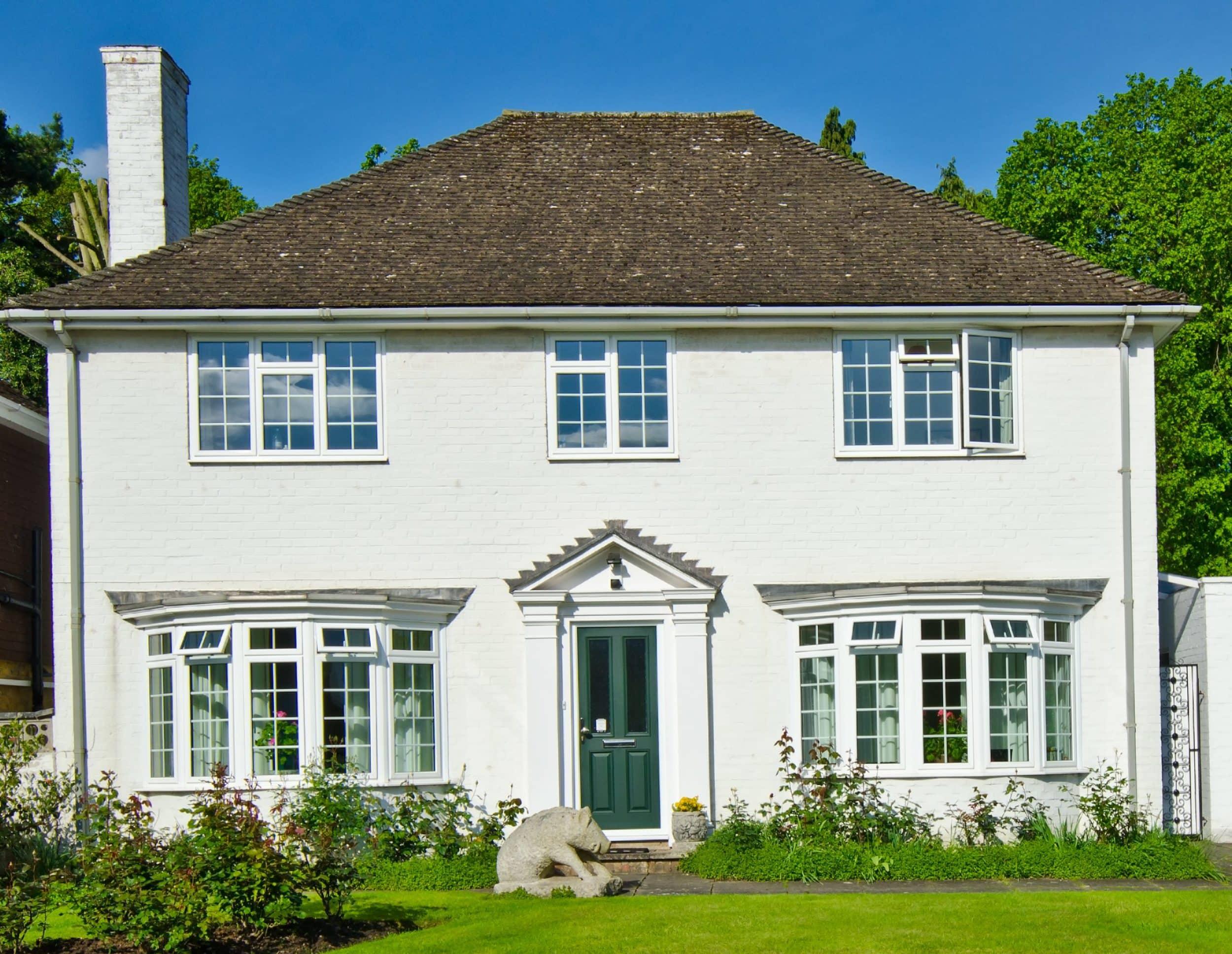 A white brick house with three white aluminium windows on the top floor, featuring a grid pattern. One window is open.