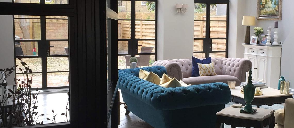 Elegant living room with velvet sofas and a large, black Aluco steel-look door and window system looking onto a patio