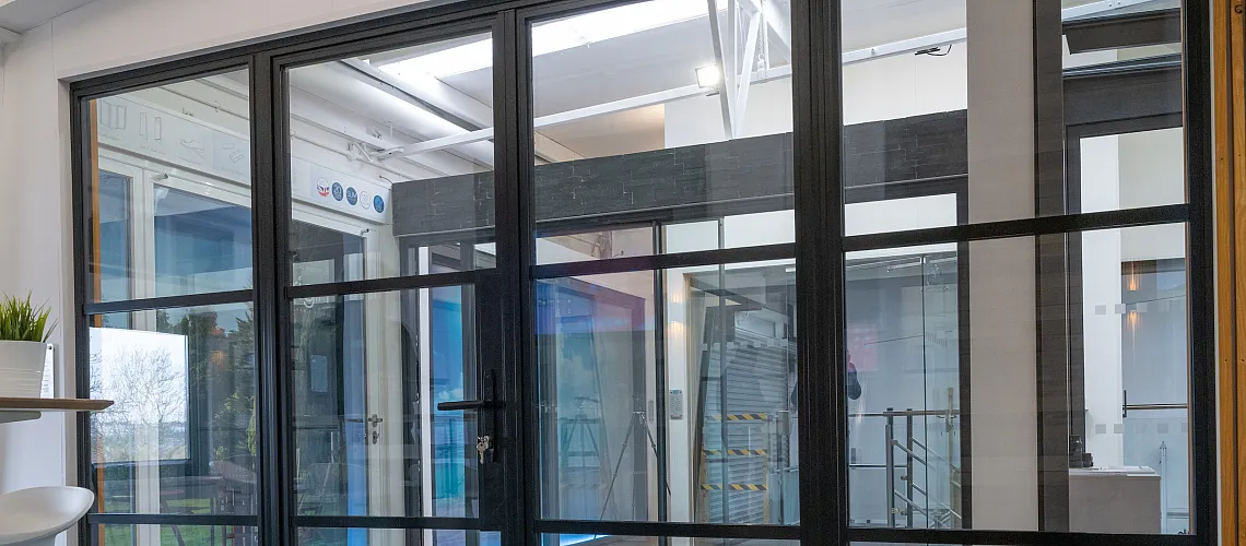 A large, black steel-replacement internal screen and door set with a grid pattern, installed in a modern showroom.