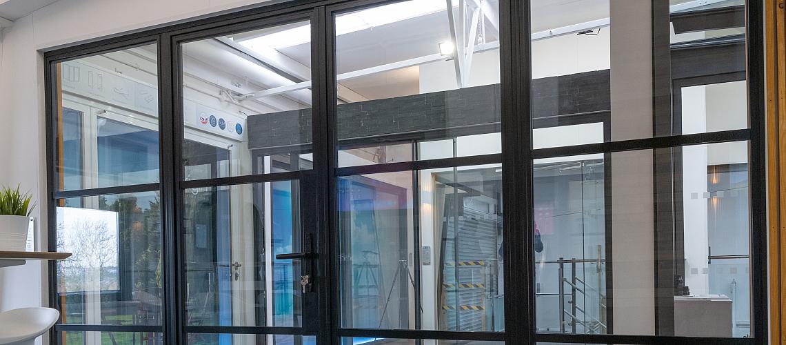 A large, black steel-replacement internal screen and door set with a grid pattern, installed in a modern showroom.
