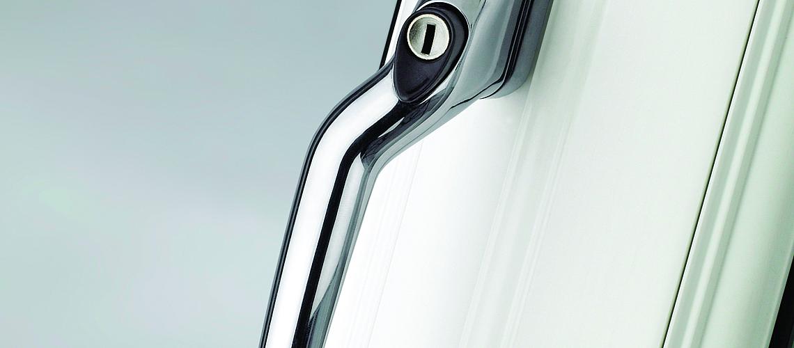 Detailed close-up of a modern, polished chrome handle with a key lock, on a white Alitherm window frame