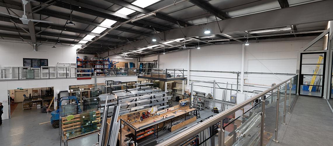 High-angle view from a mezzanine overlooking the busy FGC factory, showing workbenches and racks of window frames